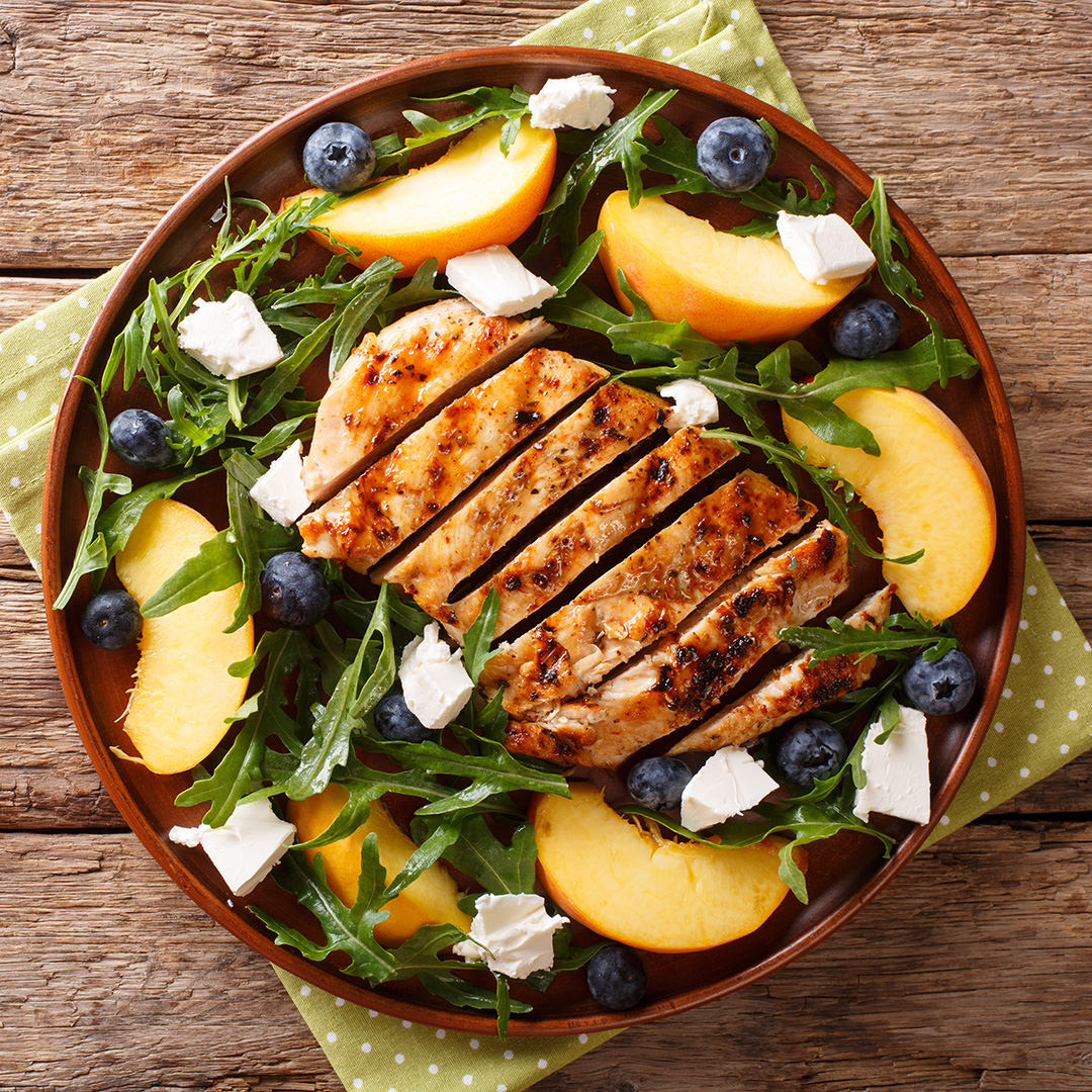 Grilled chicken breast with fresh peaches, blueberries, arugula and feta cheese close-up on a plate. Horizontal top view Grilled chicken breast with fresh peaches, blueberries, arugula and feta cheese close-up on a plate on a table. Horizontal top view from above